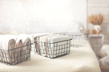 Beyaz kıyafetlerin ve keten kumaşların yatak odasındaki ağlı metal kaplarda düzgünce katlanmış ve bulanık yatağın arka planında. Mükemmel organizasyon kavramı. Reklam alanı