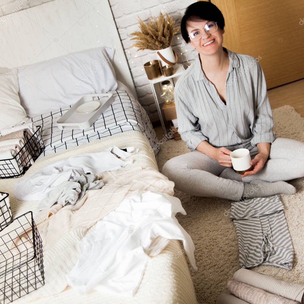 Top view of a beautiful young brunette woman folding things up on mesh metal containers while sitting in her cozy bedroom. Weekly cleaning concept