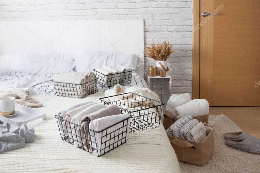 Mesh metal containers full of clothes and linen stand on the bed and on the floor in the bedroom with cup of coffee during general cleaning. Concept of updating and organizing