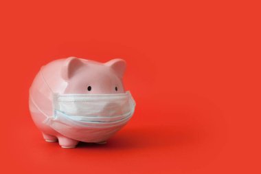 Tıbbi maskeli pembe kumbara kırmızı arka planda yarım yamalak. Salgın sırasında yaşanan finansal kriz kavramı ve para mevduatlarında düşük faiz oranları. Reklam alanı