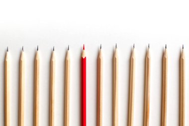 Düzgün açılmış tahta kalemler kırmızı kalemin yanındaki beyaz arka planda yan yana yatıyorlar. Ekipteki parlak yetenekli çalışan kavramı. Lider ve ideolojik. Kopyalama alanı