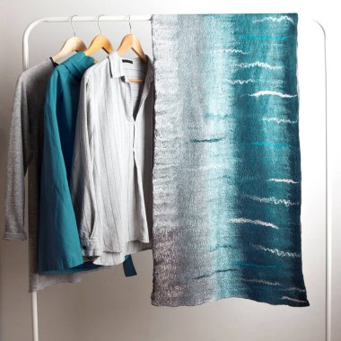 Zarif gri-yeşil ipek yünlü eşarp sergi salonundaki beyaz arka planda gri bir gök mavisi ceketin yanında asılı duruyor. Benzersiz tasarımcı şeyleri kavramı