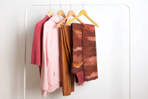 Female spring wardrobe in pink terracotta shirts and scarf hang on white hanger in the studio. Concept of changing seasonal clothes and trend color