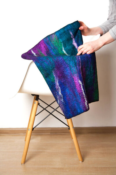 Bright blue-violet silk wool scarf made hand-made by an unidentified woman designer lies on light chair on white background. Concept of unique natural materials accessories. Copyspace