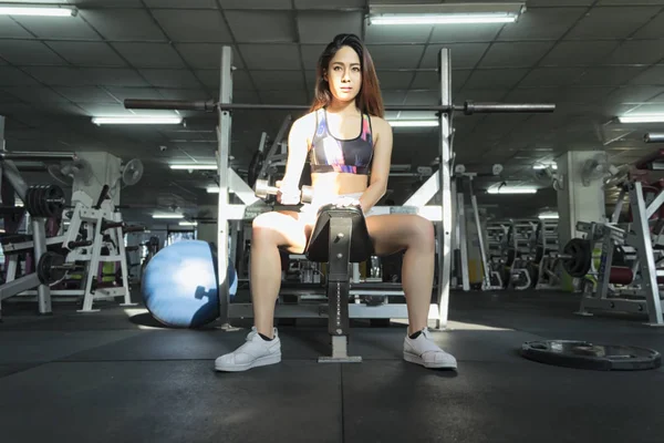 Mujer de fitness en el entrenamiento, mostrando ejercicios con mancuerna en gy — Foto de Stock