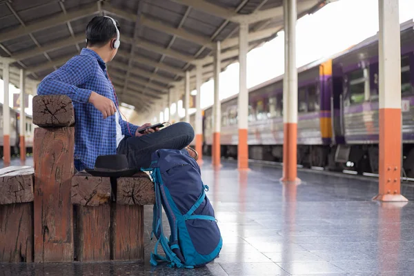 Hombre viajero con mochilero escuchando música en la estación de tren — Foto de Stock