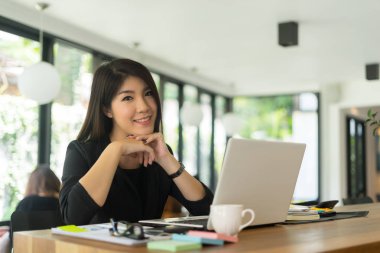 Kafede oturmuş kameraya bakan mutlu bir kadın.