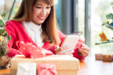 Noel Baba şapkalı bir kadın internet üzerinden akıllı telefon alışverişi yapıyor, online alışveriş yapıyor.