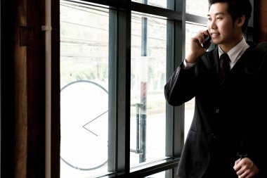 Ofis penceresinin yanında akıllı telefonu olan genç işadamı, iş konsepti