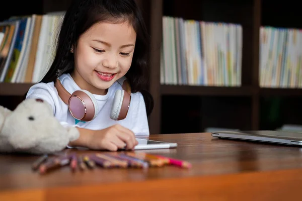 かわいい女の子の笑顔座って図書館でタブレットスマートフォンを遊んで子供の概念教育の概念 — ストック写真