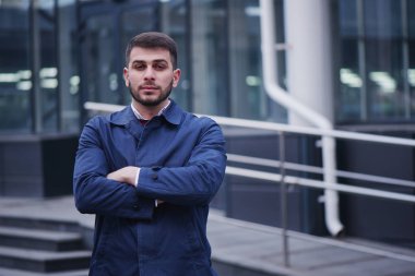 kameraya bakarak ve building yakınındaki Çapraz kollar ile ayakta mavi ceketli gülümseyen iş adamı 
