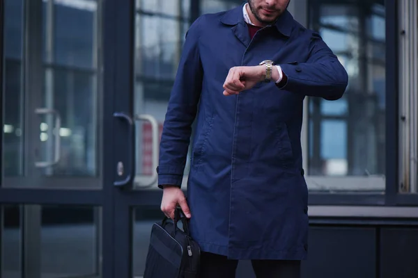 well-dressed businessman with briefcase looking at watch on hand while walking at street