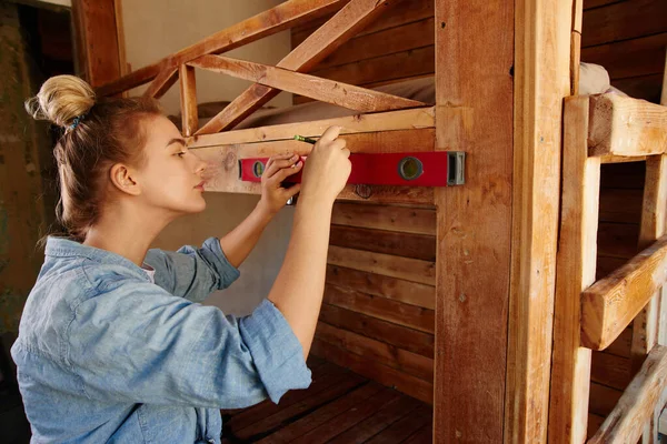 Beautiful young woman doing home renovation, observing wall alignment using building water level on wooden bunk bed background, DIY — Stock Image Beautiful Young Woman Doing Home Renovation Observing Wall Alignment Using Stock Picture