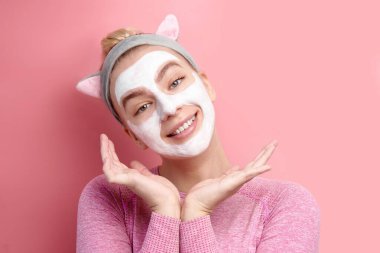 Yüzünde kozmetik beyaz maske ve pembe stüdyoda poz veren Koreli kedi kulaklığı olan sevimli genç kawaii kız.