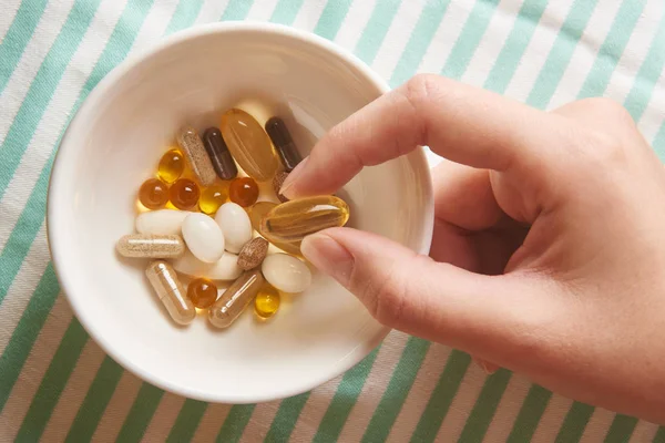 Omega-3 gelatin capsule in female hand on background of various dietary supplements, vitamins and minerals closeup