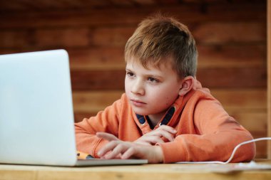 Akıllı odaklı yüzü olan bir çocuğun portresi dizüstü bilgisayarda ödev yapıyor, online okulda uzaktan eğitim görüyor.