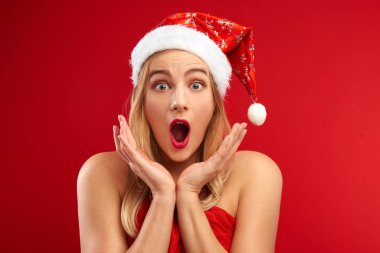 Noel Baba şapkalı şaşkın kız şaşkın kırmızı arka planda fotokopi alanı ile izole edilmiş, noel ve yeni yıl için hediyeler alma zamanı, indirimler ve satışlar