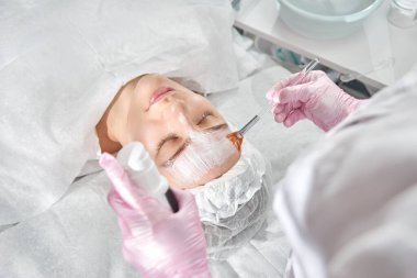 Kuafördeki profesyonel güzellik uzmanı genç bir kadın için kapsamlı yüz bakımı sağlıyor. Pore temizleme prosedürleri, tüm sezon soyma, yaşlanmayı önleyici maske