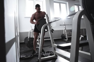 Spor salonunda kaslarını şişiren kaslı güçlü atletik adam, halterli vücut geliştirici, spor beslenme konsepti.