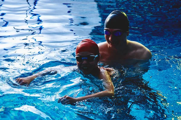 아버지 련사는 아들에게 수영을 가르치고 수영을 즐기고 푸른색 수영장에서 튀기는 — 스톡 사진