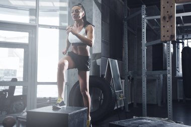 Kaslı seksi esmer kadın spor salonunda adımlarla kardiyo çalışması yapıyor.