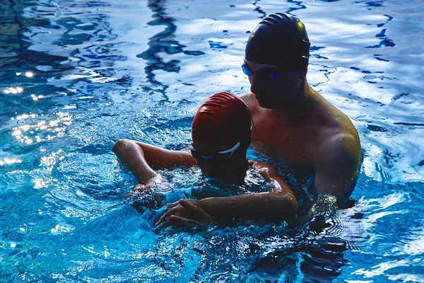 아버지 련사는 아들에게 수영을 가르치고 수영을 즐기고 푸른색 수영장에서 튀기는 — 스톡 사진