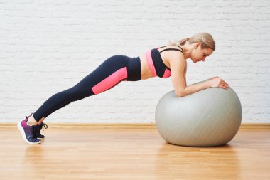 Spor yapan atletik bir kadın, arka planda izole edilmiş bir fitness topuyla sağlıklı egzersiz yapıyor. Evde ve spor salonunda egzersiz, Pilates.