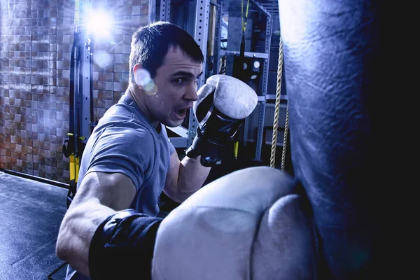 职业拳击手肌肉男子击败拳击袋在拳击手套 训练运动员在健身房 侵略性的战斗在黑暗的颜色 — 图库照片