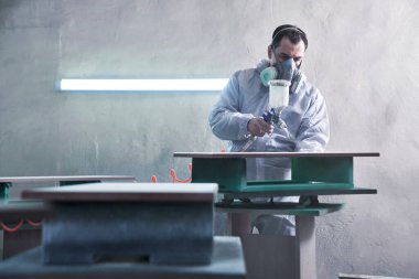 Fabrikada ahşap mobilya üretim ve üretim süreci. Tulumlu işçi ahşabı boya spreyiyle boyuyor.