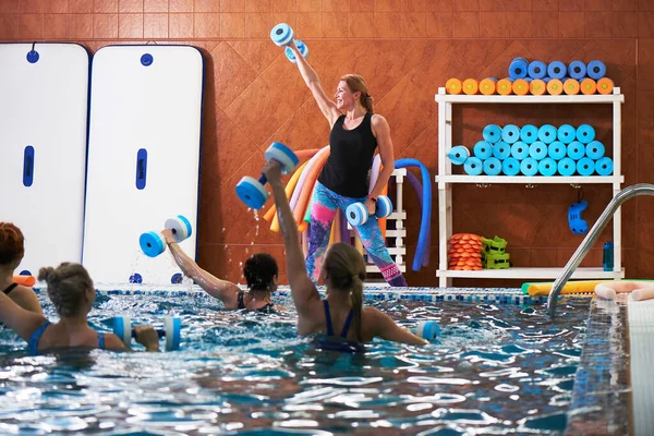 若い女の子と中年の女性は トレーナーとスイミングプールでダンベルとアクアエアロビクスを行います 水中での体重減少のためのフィットネス演習 — ストック写真