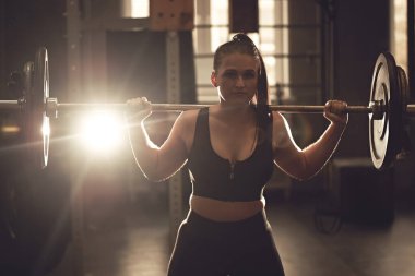 Samimi ve güçlü bir genç kadın spor salonunda halterle antrenman yapıyor, mekik çekiyor ve kaldırıyor. Gerçek Wout.