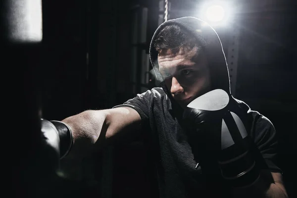 プロボクサー筋肉マンは ボクシングの手袋で袋をパンチビート ジムで選手を訓練し 暗い色で積極的な戦い クローズアップ肖像画 — ストック写真