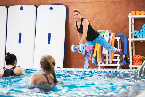 年轻女孩和中年妇女与教练一起在游泳池里用哑铃做水上运动 做健身锻炼以减轻水中的体重 — 图库照片
