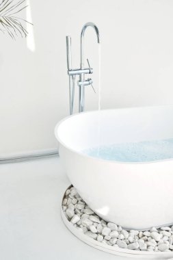 Beyaz banyo modern iç mekan. Çiçekleri, penceresi, kaplıcası olan lüks bir dekor. Küvet musluk suyuyla dolu, kimse yok.