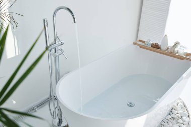 Beyaz banyo modern iç mekan. Çiçekleri, penceresi, kaplıcası olan lüks bir dekor. Küvet musluk suyuyla dolu, kimse yok.