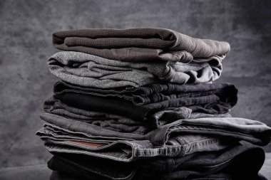 Siyah gri arka planda izole edilmiş, düzgünce katlanmış koyu renk kıyafetler yığını.