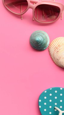 Pembe arka planda deniz kabuğu olan güneş gözlüğü ve sandaletler.