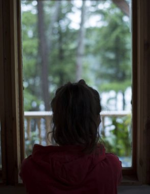 Genç kahverengi saçlı kadın ev pencere orman, yağmurlu bir günde bakarak