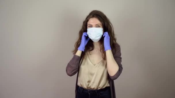 Brunetka młoda kobieta zdjąć maskę ochronną na twarz w pandemii koronawirusa na szarym tle niebieskie rękawiczki — Wideo stockowe