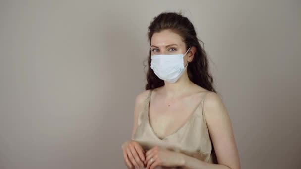 Брюнетка молодая женщина снимает защитную маску на лице в коронавирусной пандемии на сером фоне — стоковое видео