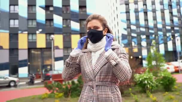 Joven hermosa chica caucásica quitarse una máscara de la cara negro aliento sonrisa durante una pandemia con guantes azules — Vídeo de stock