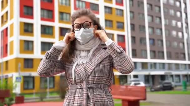 Eine junge Frau mit Brille nimmt ihre weiße Maske ab und lächelt während der Coronavirus-Pandemie — Stockvideo