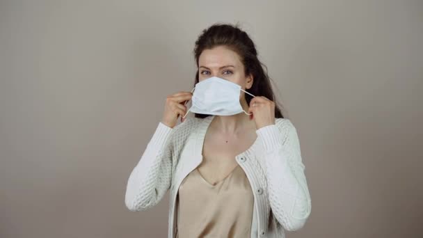 Молода жінка, одягнена в захисну маску на обличчі під час коронавірусної пандемії на сірому тлі.. — стокове відео