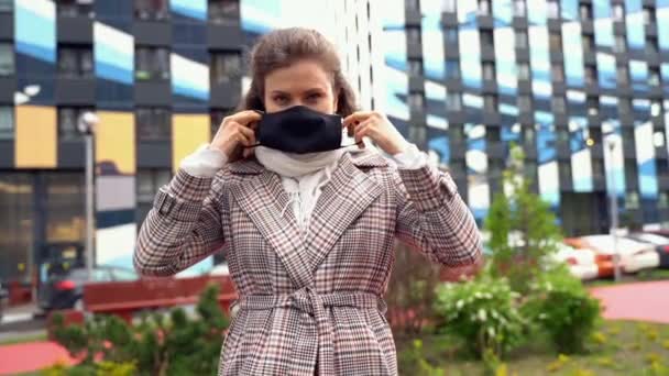 Giovane bella donna caucasica mette una maschera nera sul suo viso per proteggersi durante una pandemia — Video Stock