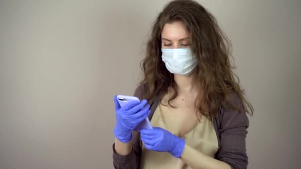 Brunette young woman in protective mask on face in coronavirus pandemic on grey background touch her phone — Stock Video