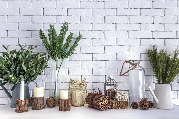 Pot de plantes, branche, fleurs, chandelles et verre de décorations de bouteilles sur fond blanc de table et de mur de briques . — Photo