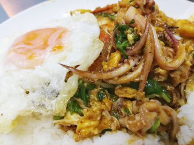 Sarı köri içinde kızarmış deniz ürünleri ya da tavada kızartılmış, kızarmış yumurta ve pirinç ile hizmet.