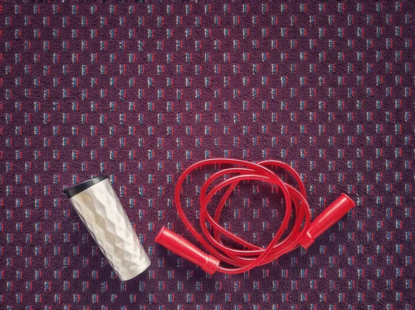 Water bottle and jumping red rope on a carpet floor at fitness gym. — Stock Photo, Image