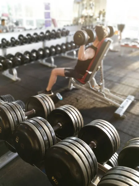 Fileiras de halteres e pessoas não identificadas estão trabalhando no ginásio de fitness . — Fotografia de Stock