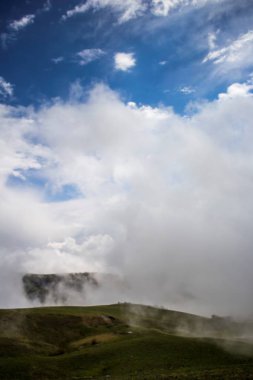 Yeşil yamaçları beyaz bulutlar tarafından sıkılır